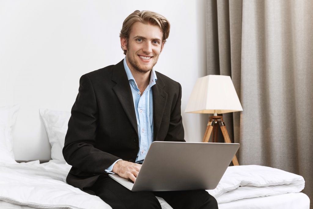 portrait-cheerful-bearded-company-director-stylish-black-suit-smiling-brightfully-working-laptop-computer-comfortable-hotel-room-during-business-trip-1024x683